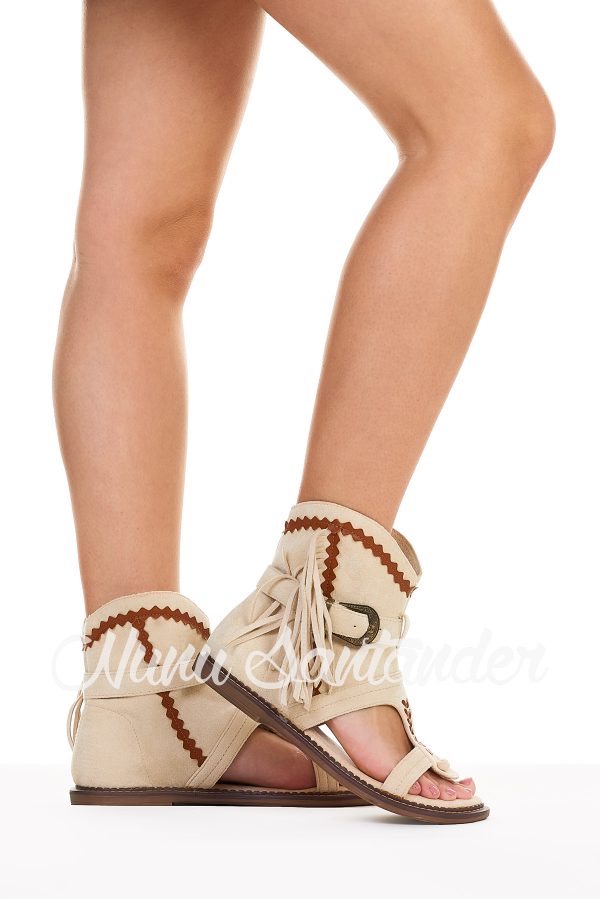 Sandalia estilo bota de antelina transpirable. Trae caña baja decorada con trenzados, con cierre mediante hebilla y flecos en el lateral.