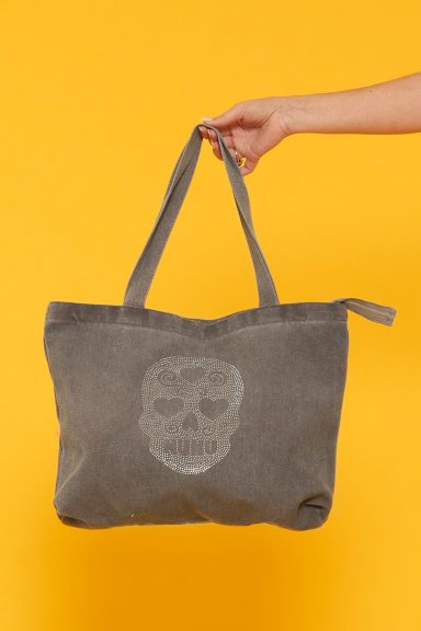 Un bolso estilo tote bag que tiene cierre de cremallera y diseño hecho y formado por strass de una calavera.