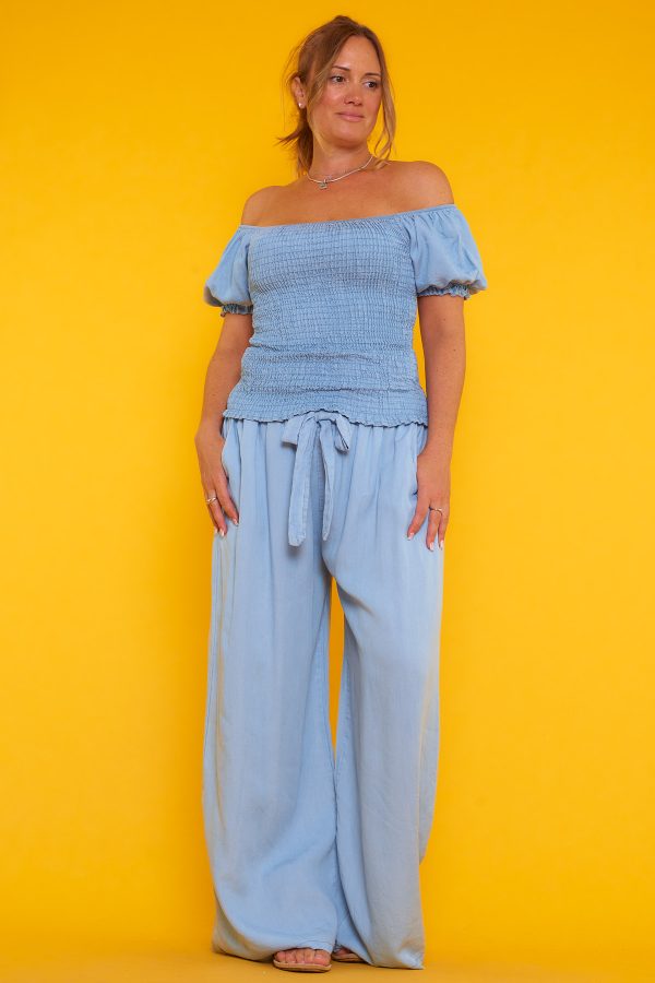 Una blusa que tiene escote palabra de honor y nido de abeja. Tiene goma elástica en los bordes del escote y las mangas.