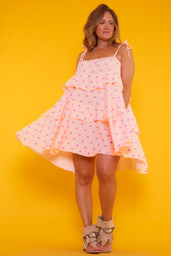 Un vestido corto elástico que tiene volantes y tirantes que se regulan por medio de un nudo. Tiene goma elástica en los bordes superiores.