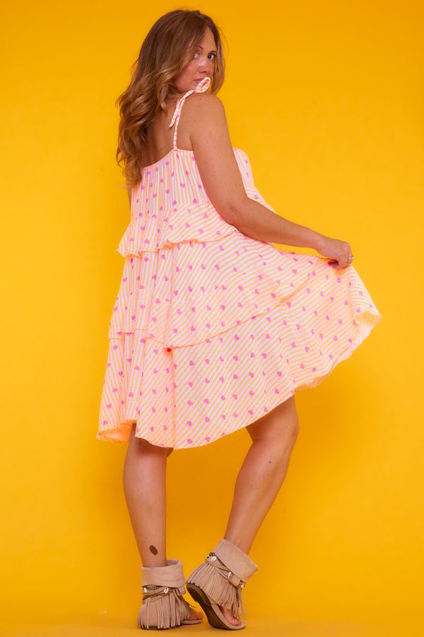 Un vestido corto elástico que tiene volantes y tirantes que se regulan por medio de un nudo. Tiene goma elástica en los bordes superiores.