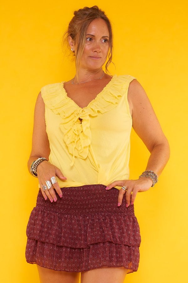 Una blusa elástica que no tiene mangas. Tiene escote en pico con volantes y cordones para hacer un nudo decorativo o ajustar a medida.
