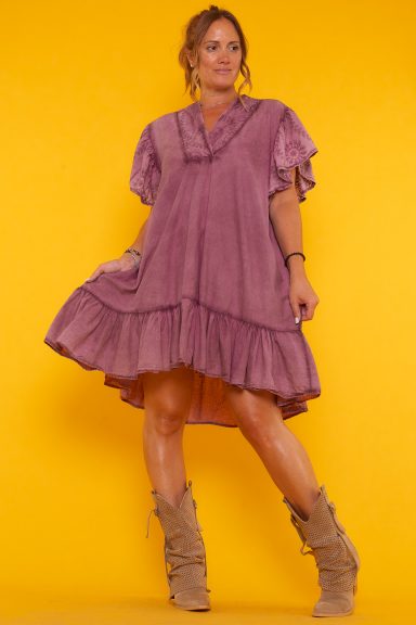 Un vestido corto que tiene volantes en la parte inferior y en las mangas. Tiene escote en pico y un corte asimétrico.