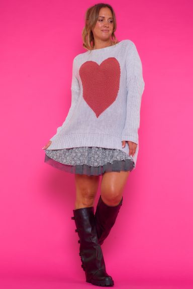 Un jersey de punto que es elástico de manga larga que tiene un diseño de un corazón en la parte frontal y un corte asimétrico.