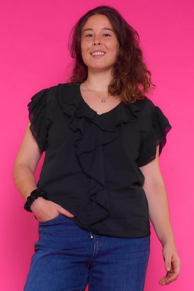 Blusa Con Volantes Malaca Una blusa de manga corta que tiene un tejido extremadamente suave y ligero. La prenda tiene volantes en todo su escote y en sus mangas.