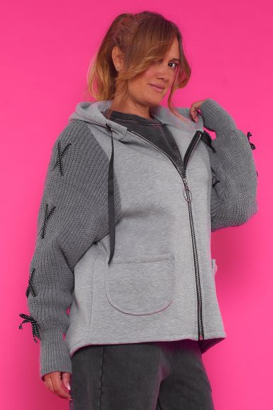 Una sudadera elástica asimétrica que tiene capucha, dos bolsillos frontales, un cierre por medio de cremallera y sus mangas de punto.